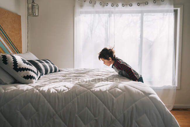 Menino pulando em uma cama em casa — Fotografia de Stock