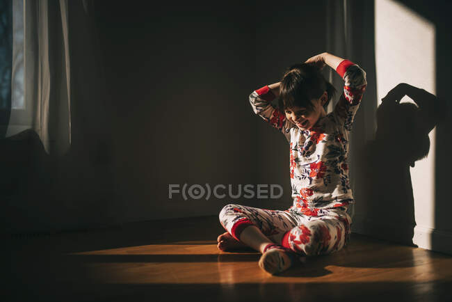 Девушка сидит на полу в пижаме с руками в волосах — стоковое фото