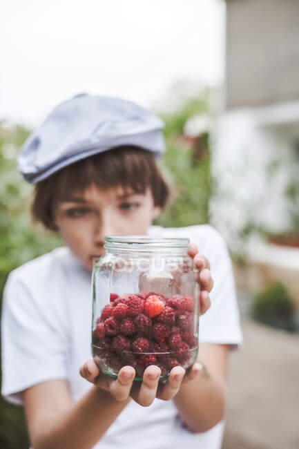 Close-up portrait of Boy holding a jar of raspberries — Stock Photo