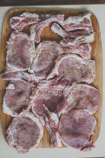 Bifes de porco crus com especiarias em uma tábua de corte — Fotografia de Stock