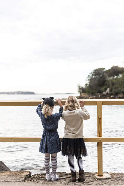Dos chicas sosteniendo una barandilla con vistas al mar, Sydney, Nueva Gales del Sur, Australia - foto de stock