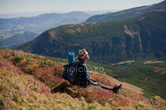 Mujer sentada en la ladera de la montaña mirando a la vista, Ucrania - foto de stock
