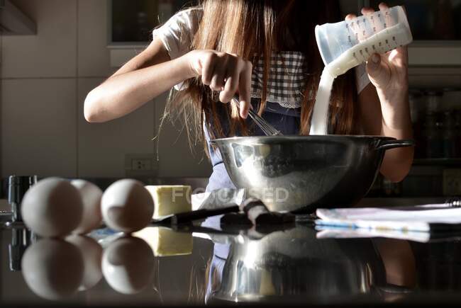 Teenage girl standing in kitchen baking a cake — Stock Photo