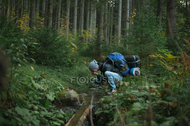 Hombre agachado por un arroyo de agua potable, - foto de stock