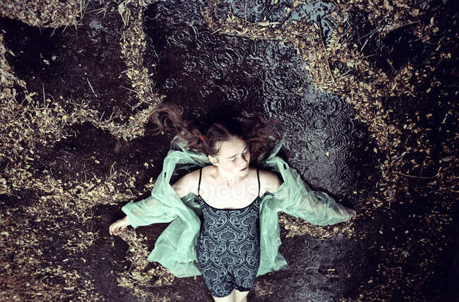 Vista aérea de una chica acostada en el suelo bajo la lluvia - foto de stock