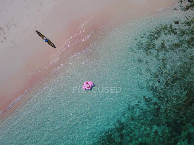 Vista aérea de una mujer en un flotador de flamenco inflable rosa, Pink Beach, East Nusa Tenggara, Indonesia - foto de stock