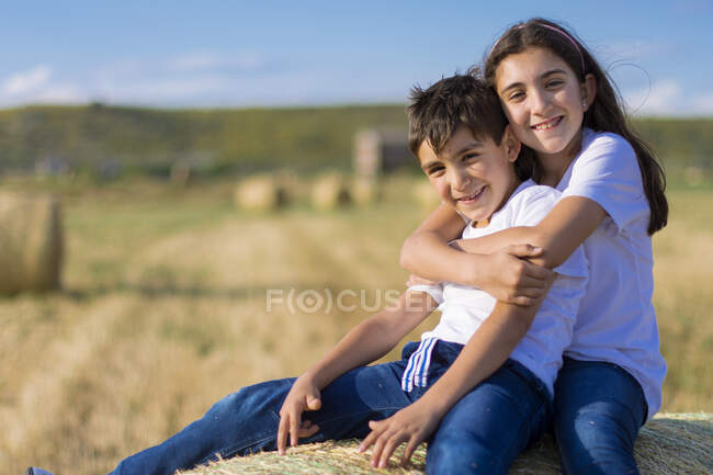 Дівчина сидить на тюці, обмотуючи брата — стокове фото