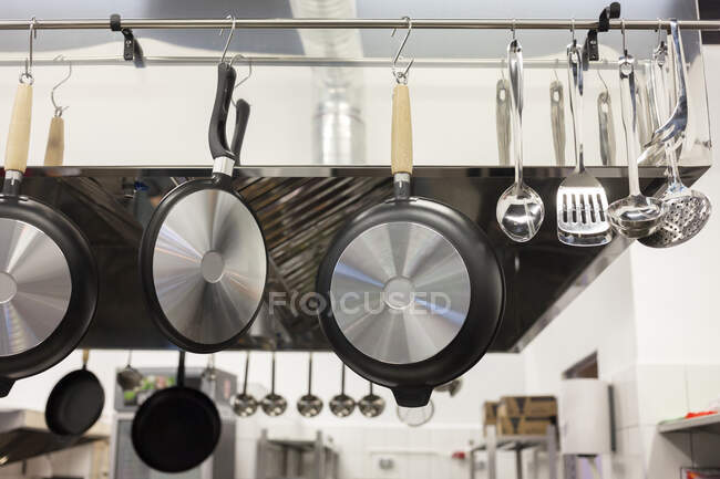 Frigideiras, panelas e utensílios pendurados em uma cozinha — Fotografia de Stock