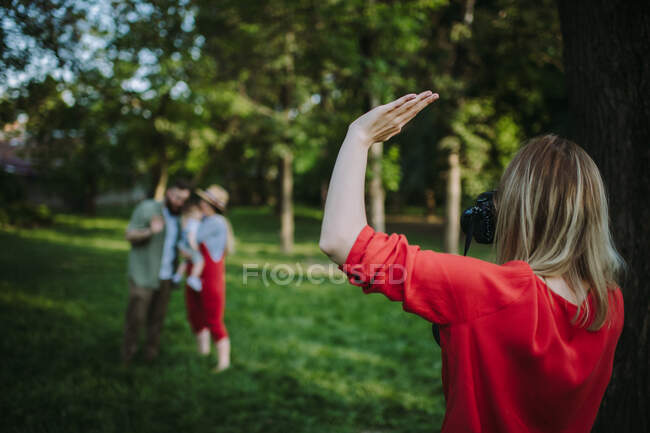 Mujer de pie en el parque saludando a una madre y un padre con su hijo - foto de stock