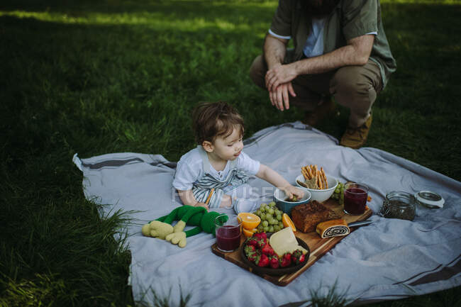 Boy sitting on a picnic blanket eating next to his father — Stock Photo