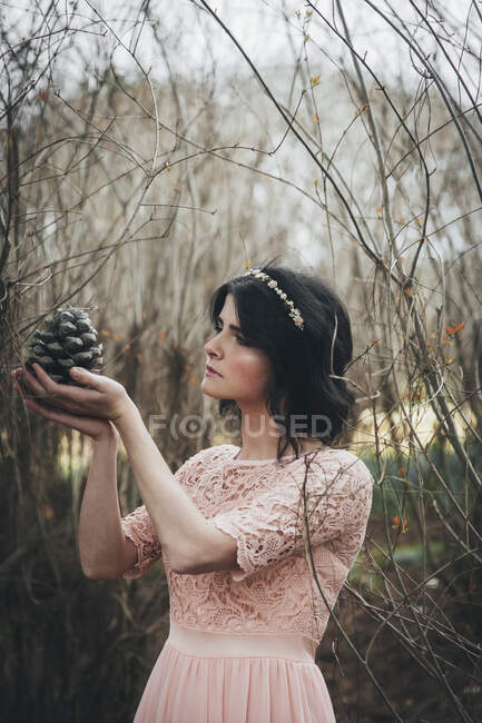 Жінка стоїть в лісі тримає сосновий конус — стокове фото