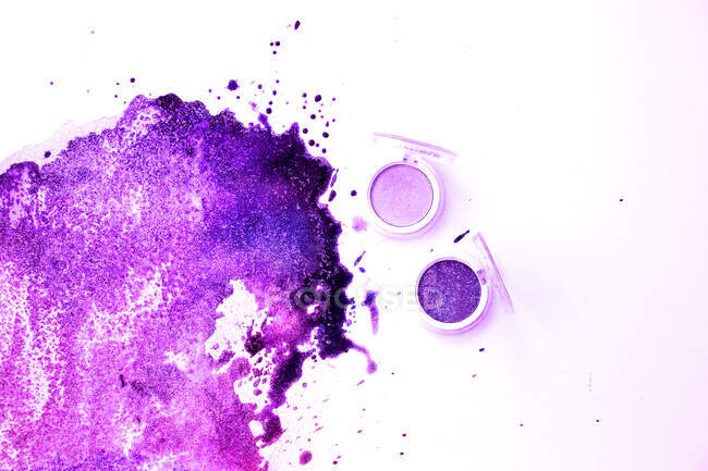 Purple eyeshadows with splashes on white background — Stock Photo