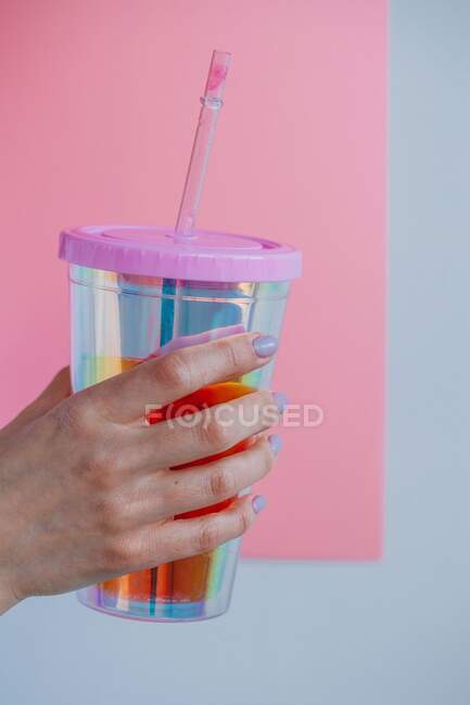 Mano de mujer sosteniendo una taza de plástico con una pajita para beber - foto de stock