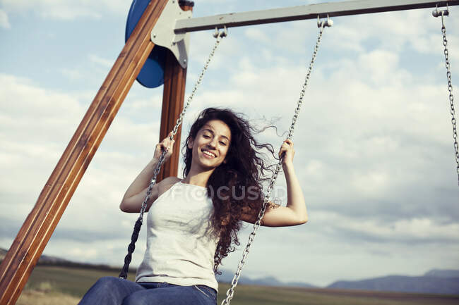 Woman with windswept hair sitting on a swing — Stock Photo