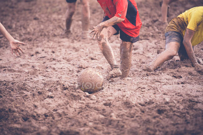 Dois meninos jogando futebol na lama com seus amigos — Fotografia de Stock
