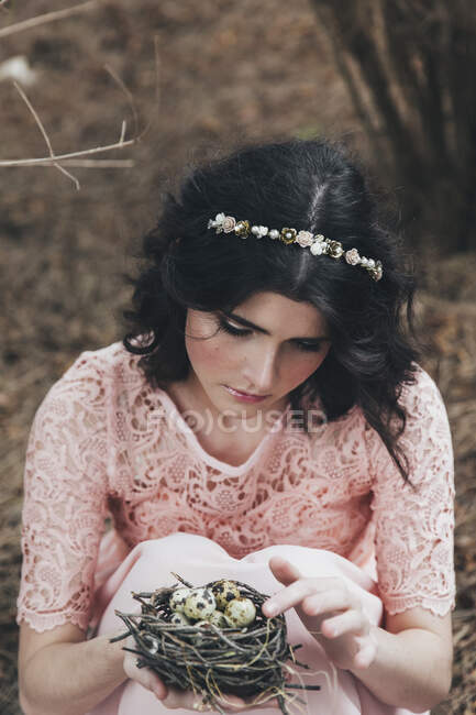 Жінка сидить у лісі тримає пташине гніздо з перепелиними яйцями — стокове фото