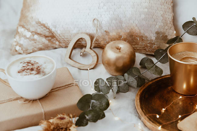 Closeup view of Cappuccino, wrapped gift and ornaments on a bed — Stock Photo