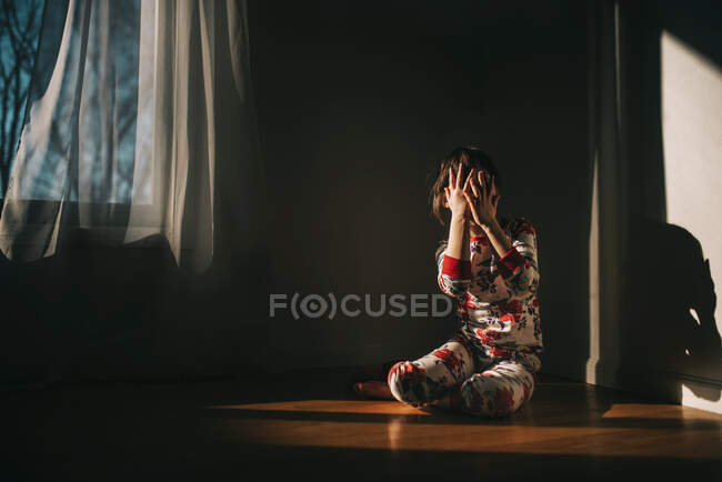 Mädchen sitzt im Schlafanzug auf dem Boden und hält die Hände vor dem Gesicht — Stockfoto