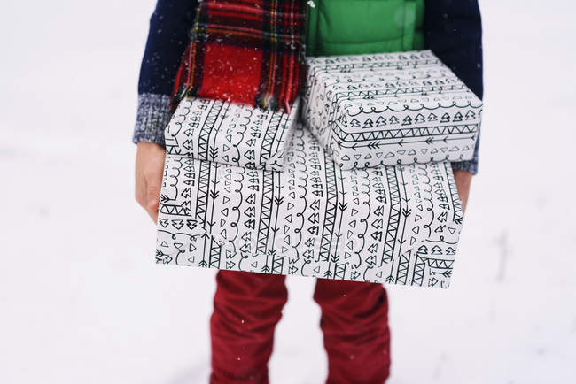 Image recadrée de garçon debout dans la neige portant des cadeaux de Noël — Photo de stock