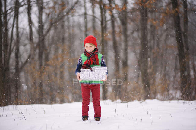 Boy standing in snow carrying Christmas gifts — Stock Photo