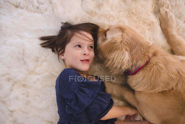 Девочка лежит на полу и играет со своей золотой собакой-ретривером — стоковое фото