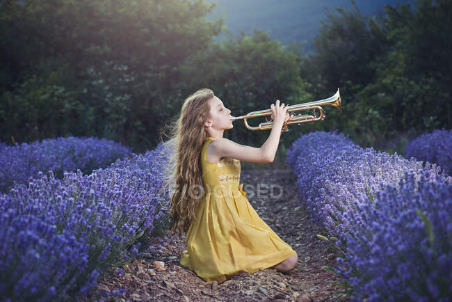 Mädchen sitzt in einem Lavendelfeld und spielt eine Trompete — Stockfoto