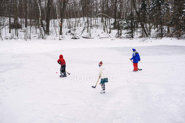 Tres niños jugando hockey sobre hielo - foto de stock