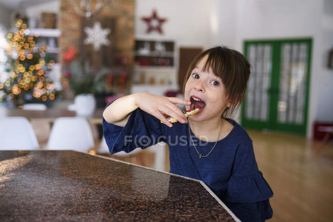 Girl standing in a kitchen eating a Christmas cookie — Stock Photo