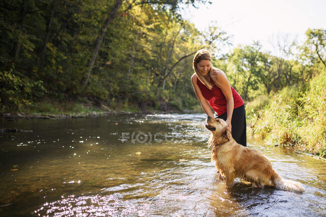 Donna in piedi in un fiume con un cane golden retriever — Foto stock