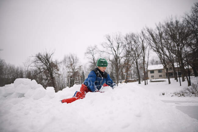 Мальчик строит снежную крепость в саду — стоковое фото