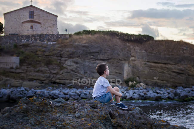 Niño sentado junto a un río al atardecer, Bulgaria - foto de stock
