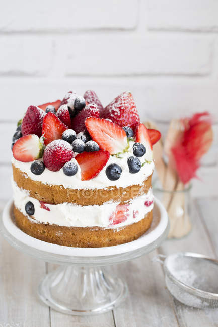 Gâteau éponge aux fraises, bleuets et crème sur un stand de gâteau — Photo de stock