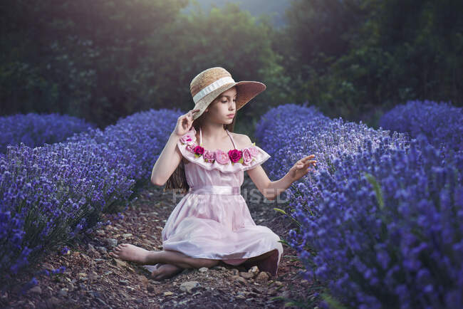 Дівчина в солом'яному капелюсі сидить у лавандовому полі — стокове фото
