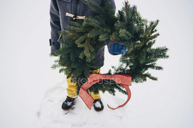 Imagem cortada de menino de pé na neve segurando uma grinalda de Natal — Fotografia de Stock