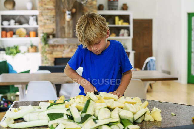 Garçon debout dans la cuisine hacher la courge — Photo de stock