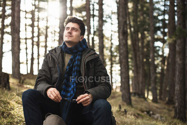 Man sitting in forest holding sunglasses — Stock Photo