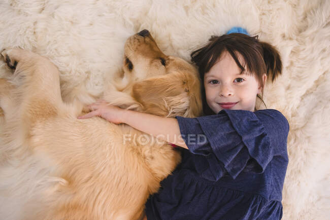 Girl lying on floor playing with her golden retriever dog — Stock Photo