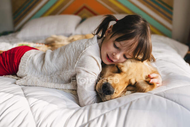 Jeune fille jouant avec le chien sur un lit — Photo de stock