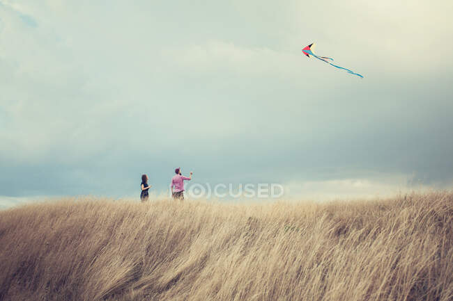 Casal de pé em uma colina voando um papagaio — Fotografia de Stock