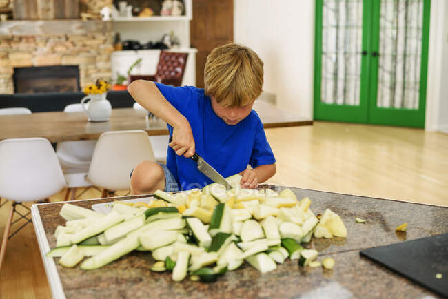 Boy standing in kitchen chopping squash — Stock Photo