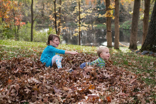 Jovem menino e menina brincando nas folhas — Fotografia de Stock