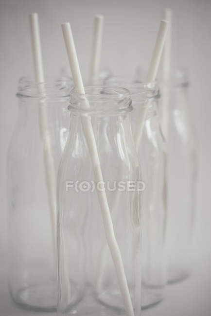 Vista de primer plano de cinco botellas de vidrio con pajitas para beber - foto de stock