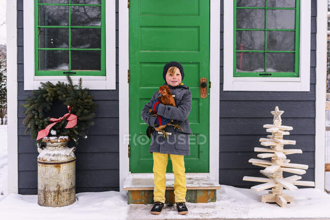 Boy standing outside a house holding a chicken — Stock Photo