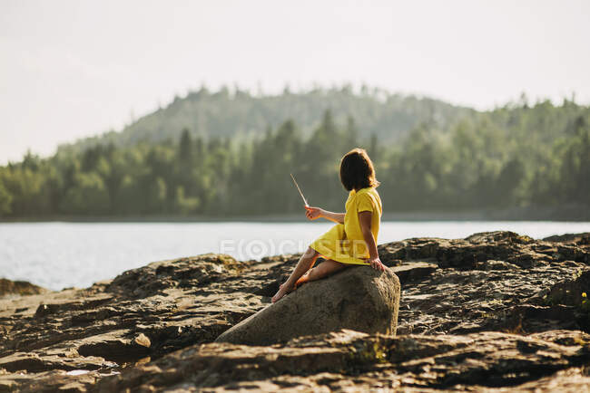 Giovane ragazza che gioca sulle rocce vicino a un lago — Foto stock