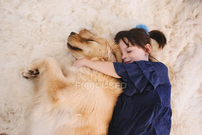Chica durmiendo en una alfombra con su perro recuperador de oro - foto de stock