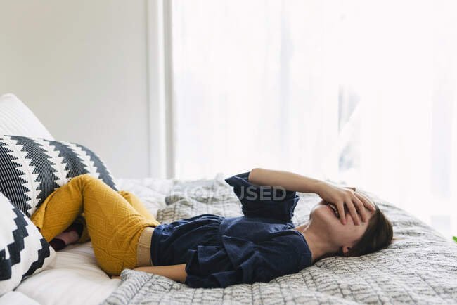 Menina deitada em sua cama rindo com a mão cobrindo os olhos — Fotografia de Stock