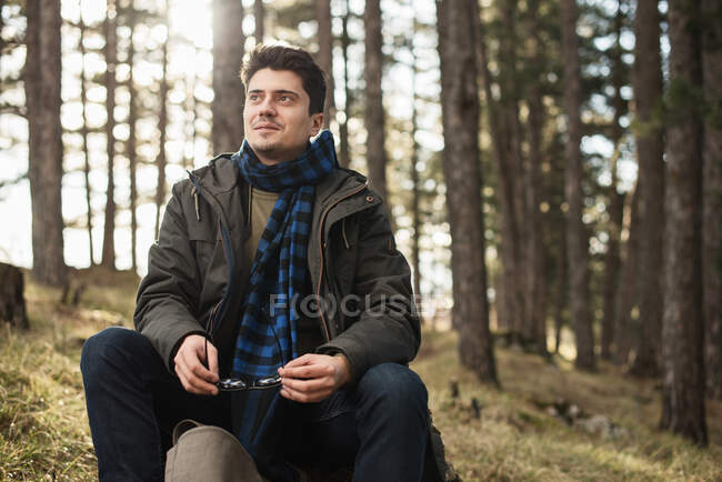 Man sitting in forest holding sunglasses — Stock Photo