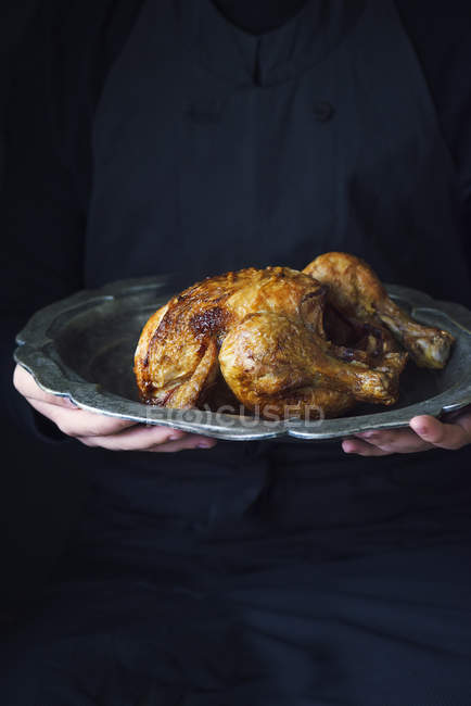 Persona che tiene un pollo arrosto su un piatto di peltro — Foto stock