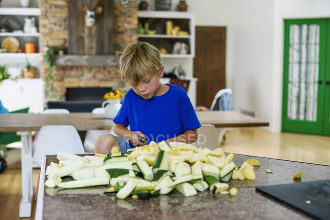 Мальчик, стоящий на кухне и рубящий сквош — стоковое фото