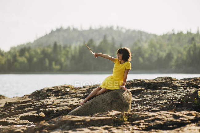 Giovane ragazza che gioca sulle rocce vicino a un lago — Foto stock